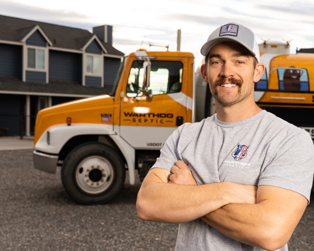 Man smiling near septic truck and house.